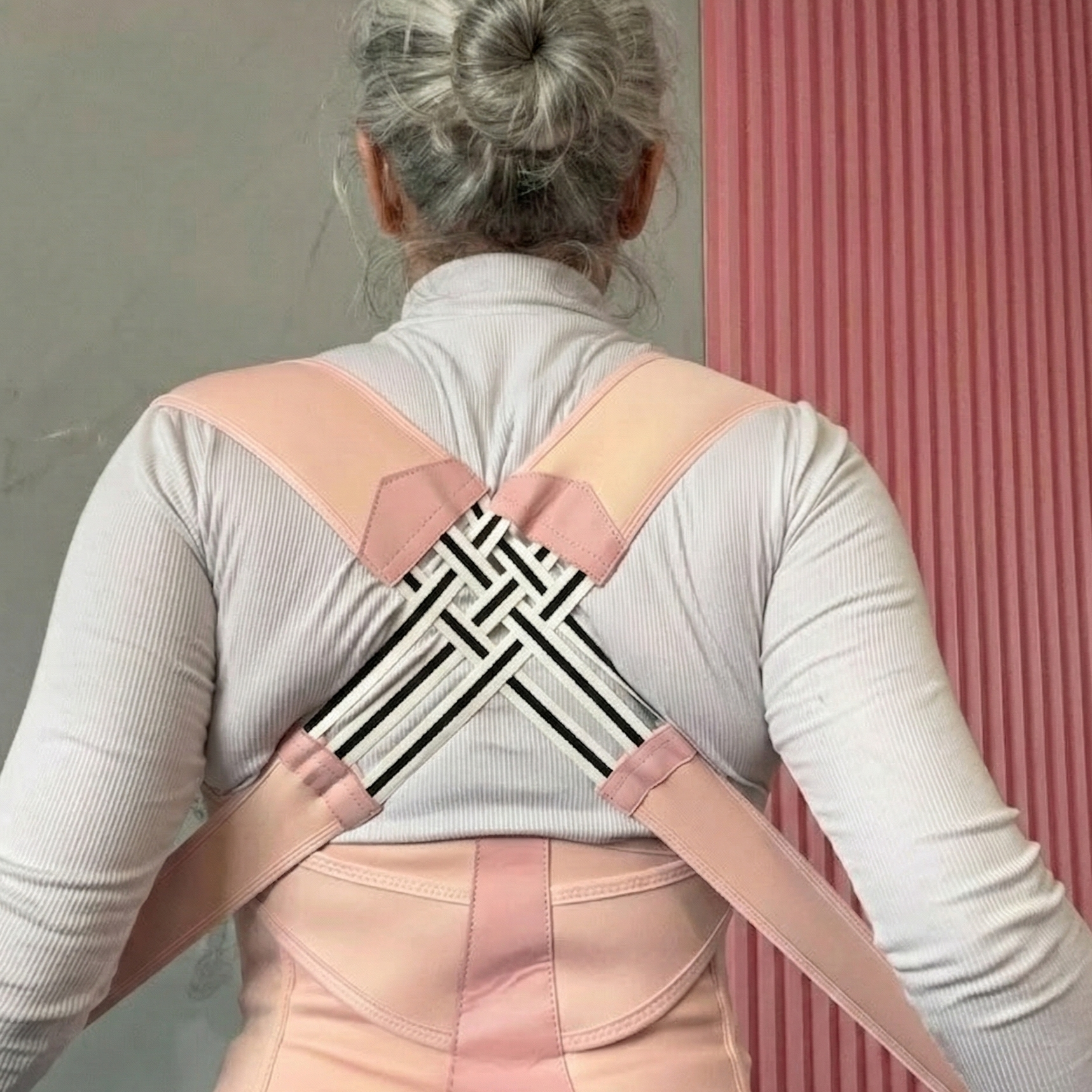 Person wearing a back brace against a pink and gray wall.